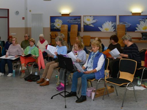 Eine Gruppe von Frauen singt gemeinsam, einige halten Notenblätter in den Händen.