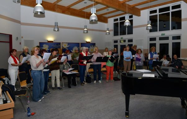 Eine Gruppe von Frauen singt gemeinsam, einige halten Notenblätter in den Händen.