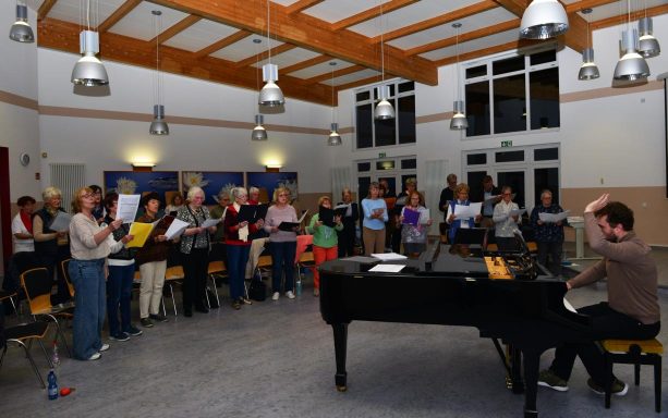 Eine Gruppe von Frauen singt gemeinsam, einige halten Notenblätter in den Händen.