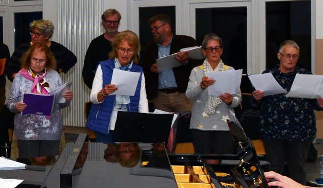 Eine Gruppe von Frauen und Männern singen gemeinsam, einige halten Notenblätter in den Händen.