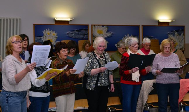 Eine Gruppe von Frauen singt gemeinsam, einige halten Notenblätter in den Händen.