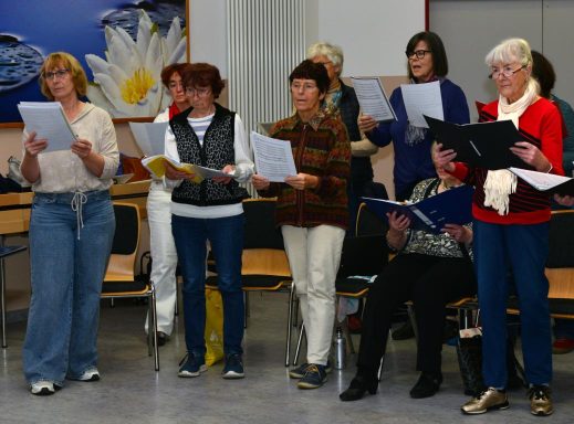 Eine Gruppe von Frauen singt gemeinsam, einige halten Notenblätter in den Händen.