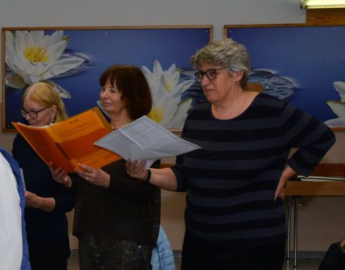 Eine Gruppe von Frauen singt gemeinsam, einige halten Notenblätter in den Händen.