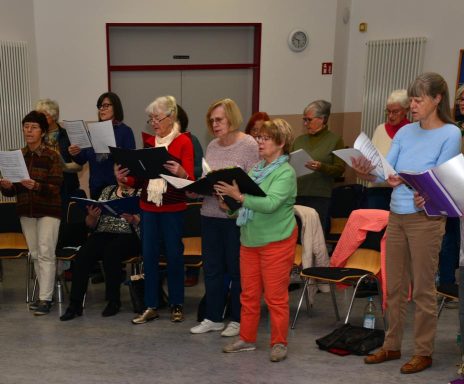 Eine Gruppe von Frauen singt gemeinsam, einige halten Notenblätter in den Händen.