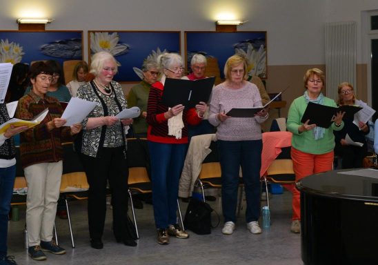 Eine Gruppe von Frauen singt gemeinsam, einige halten Notenblätter in den Händen.