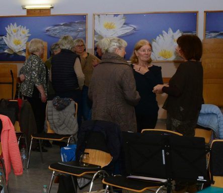 Menschen stehen in Gruppen und unterhalten sich in einem Raum mit Blumenmotiven.