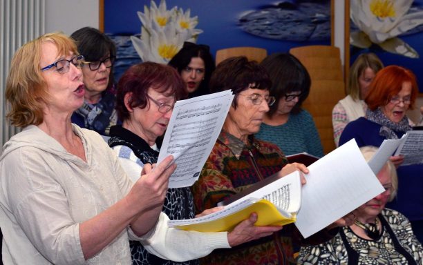 Eine Gruppe von Frauen singt gemeinsam, einige halten Notenblätter in den Händen.