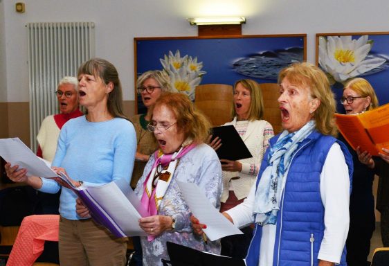 Eine Gruppe von Frauen singt gemeinsam, einige halten Notenblätter in den Händen.