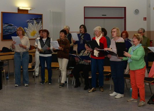 Eine Gruppe von Frauen singt gemeinsam, einige halten Notenblätter in den Händen.